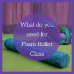 a blue foam roller lying on a green pilates mat in front of a pile of other pilates props: hand weights, massage ball, 23cm squishy ball, resistance band and a couple of head cushions in a wicker basket. All the props are in colours of purple or turquise